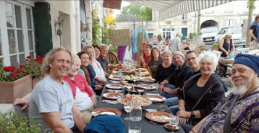 People sitting around a long table in front of a restaurant in France.