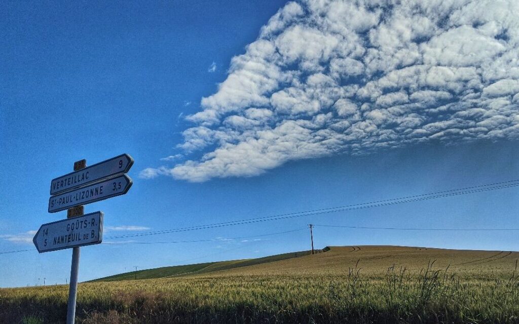 A signpost in front of fields and a blue sky.
