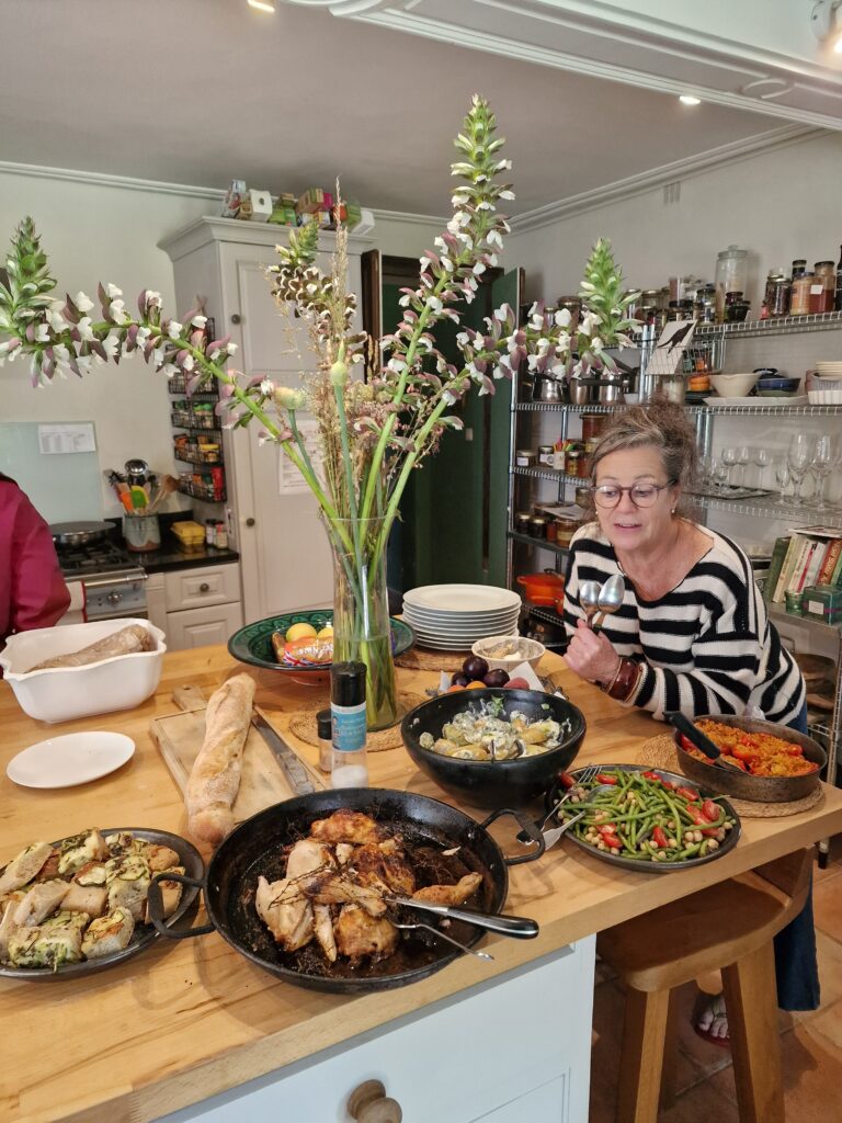 A table with plates of food and a person holding spoons.