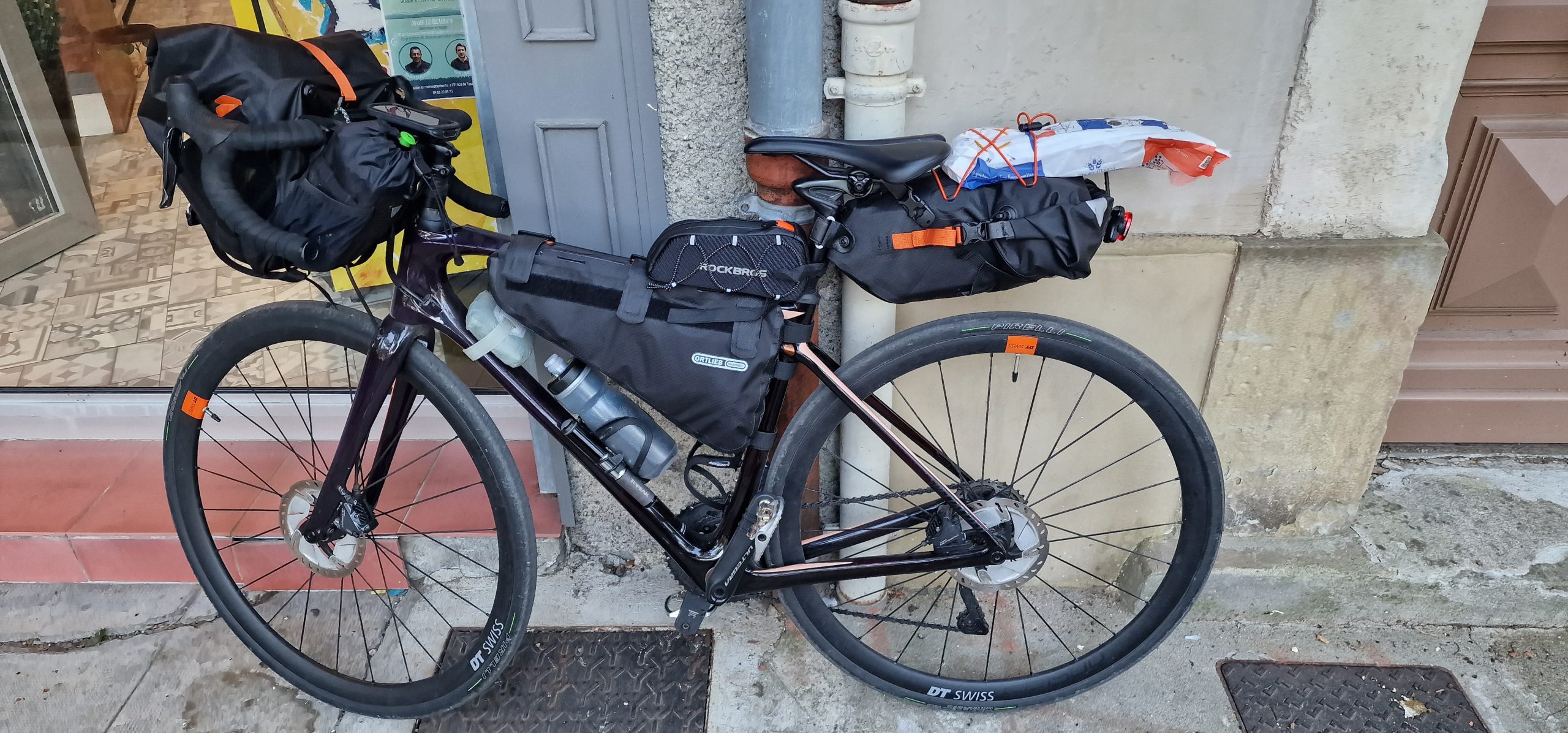 A touring bicycle packed with bags leaning against a wall outside a shop.